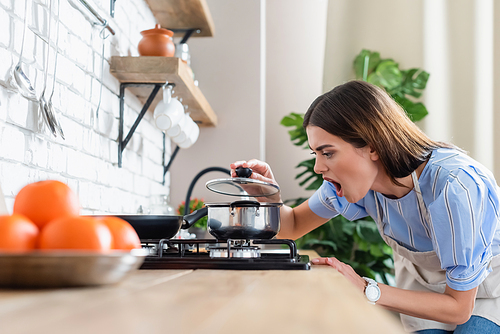 upset young adult woman cooking near burner in modern kitchen