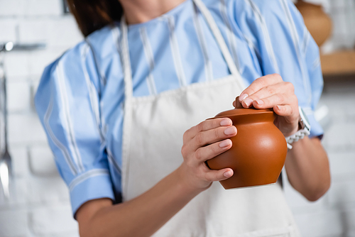 partial view of young adult woman holding clay pot in hands in kitchen