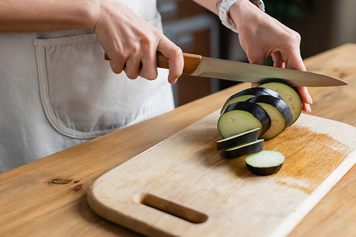 close up view of female hands cutting eggplant on chopping board in kitchen