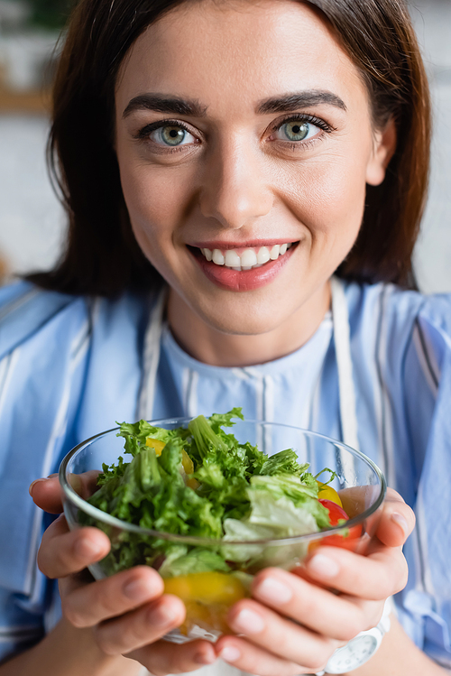 portrait of smiling young adult woman holding fresh vegetables salad in hands on blurred background
