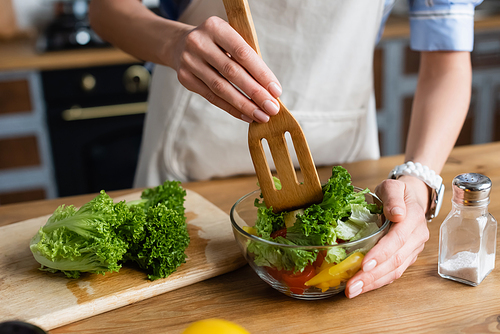 partial view of young adult woman mixing vegetables salad with spatula in kitchen