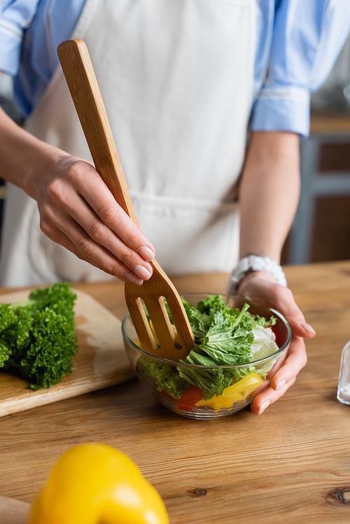 partial view of young adult woman mixing fresh vegetables salad with spatula in kitchen