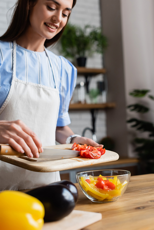 young adult woman putting sliced cherry tomatoes into vegetables salad in modern kitchen