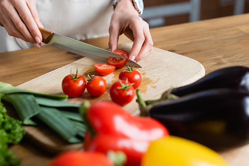 partial view of young adult woman cutting cherry tomatoes on chopping board in modern kitchen