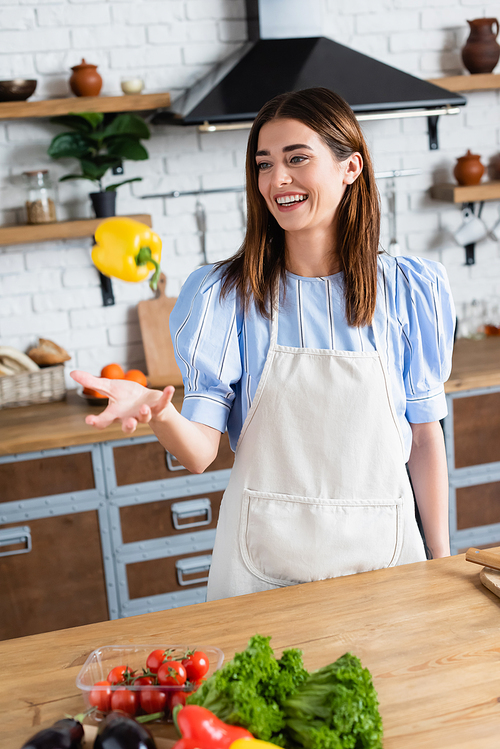 smiling young adult woman throwing yellow pepper into air in kitchen