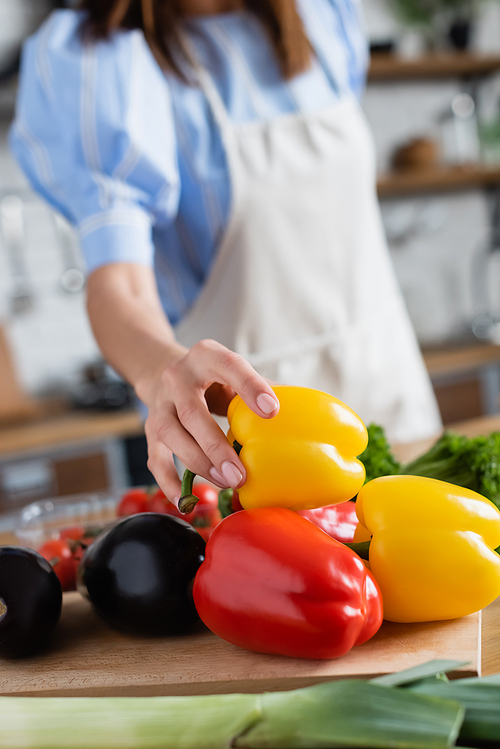 partial view of young adult woman touching yellow pepper in kitchen