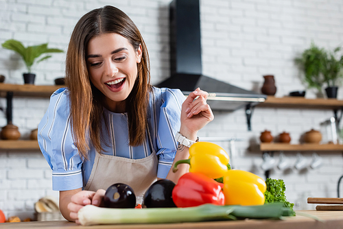 positive young adult woman looking at fresh vegetables on table in kitchen