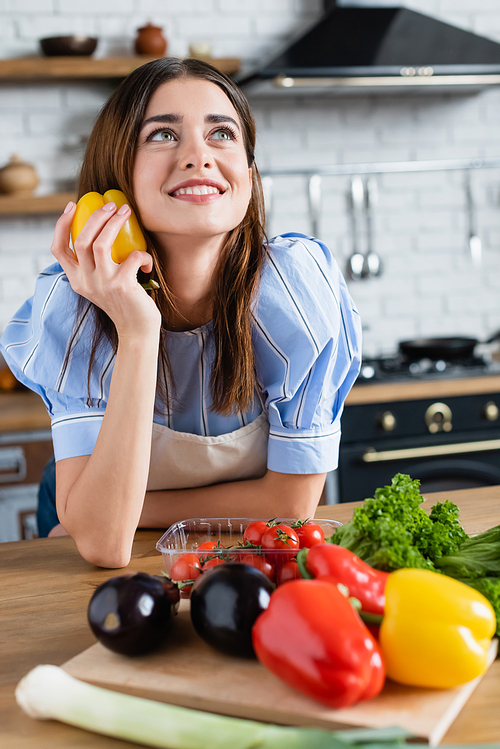 dreamy young adult woman holding fresh yellow pepper in hand in kitchen