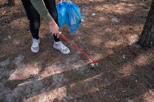 cropped view of volunteer holding pick up tool near rubbish in forest