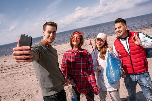 happy young man taking selfie with friends while picking up trash