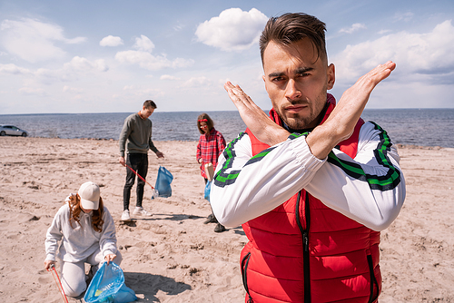 man showing stop gesture near group of volunteers picking up trash, ecology concept