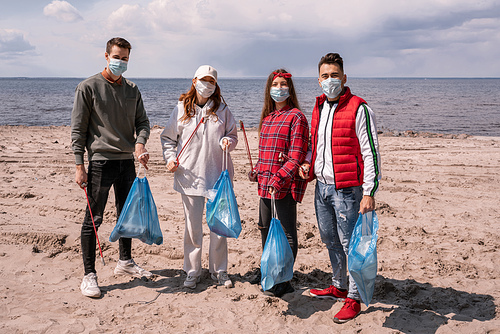 young women and men in medical masks holding trash bags and grabbers outside, pick up trash concept