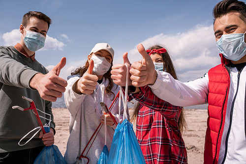 young volunteers in medical masks holding trash bags and grabbers while showing thumbs up, pick up trash concept