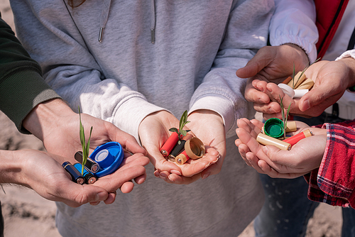 cropped view of volunteers holding batteries, plastic bottle caps and green plants in hands