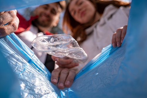 plastic cup falling in trash bag near blurred volunteers
