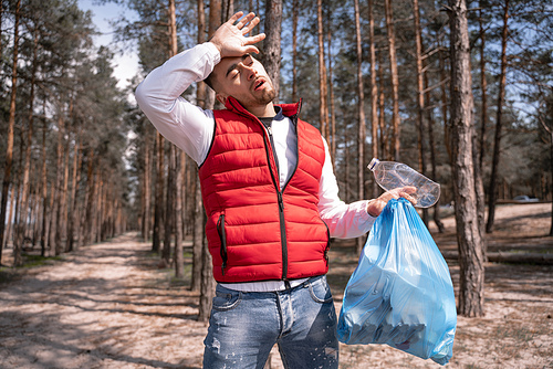 tired man holding blue trash bag in forest