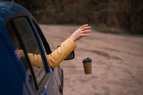 cropped view of man throwing away empty disposable cup from blue car