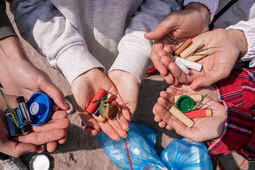 cropped view of volunteers holding batteries, bottle caps and green plants in hands