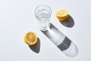transparent glass with water near lemon halves on white background