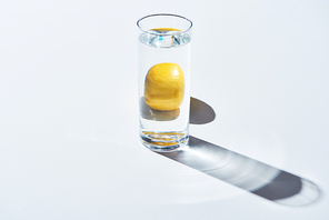 transparent glass with water and whole lemon on white background