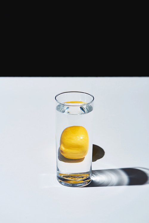 transparent glass with water and whole lemon on white surface isolated on black