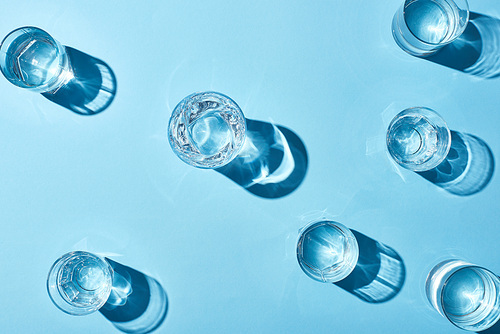 top view of transparent glasses with clear water on blue background