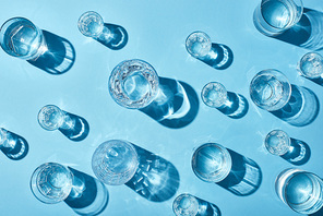 top view of transparent glasses with clear water and shadows on blue background