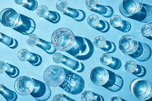 top view of glasses with clear water and shadows on blue surface
