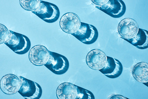 top view of glasses with pure water and shadows on blue surface