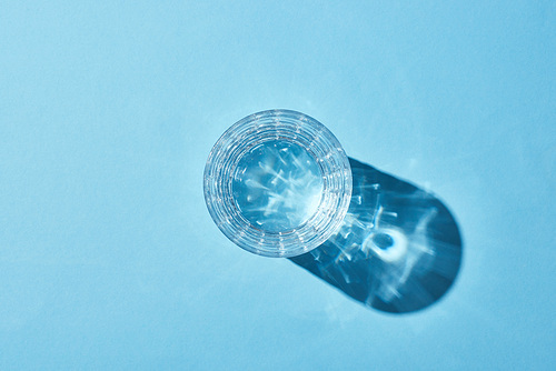 top view of glass with clear water on blue background with shadow