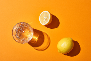 top view of glass with water near yellow lemons on orange background
