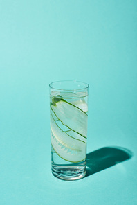 transparent glass with pure water and cucumber slices on turquoise background