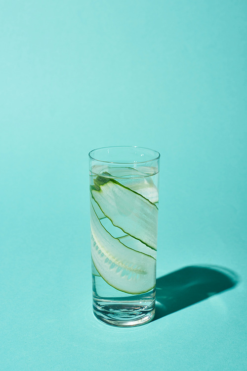 transparent glass with pure water and cucumber slices on turquoise background