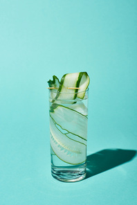 transparent glass with fresh water and cucumber slices on turquoise background