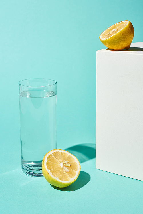 transparent glass with pure water near lemon halves on turquoise background