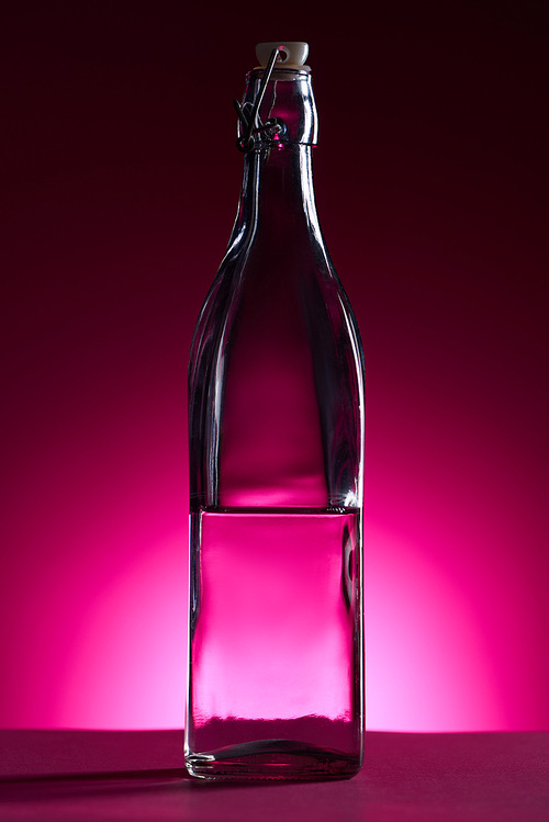 transparent bottle with water on pink background with back light