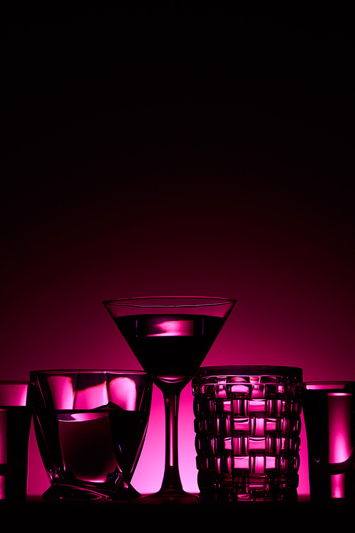 transparent glasses with liquid on dark background with pink illumination
