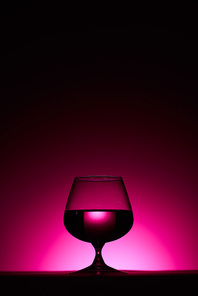 transparent glass with liquid on dark background with pink illumination