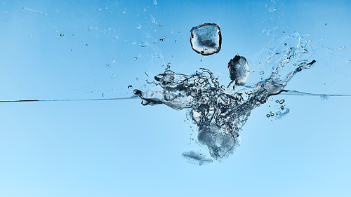 transparent water with falling ice cubes and splash on blue background