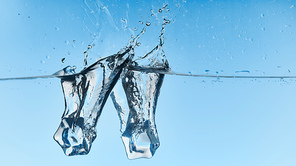 clear water with falling ice cubes and splash on blue background