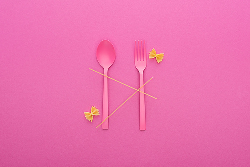 pink plastic spoon and fork, spaghetti and two uncooked farfalle pasta isolated on pink