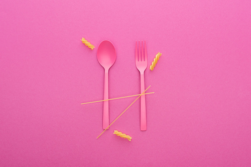 pink plastic spoon and fork and two different kinds of pasta isolated on pink