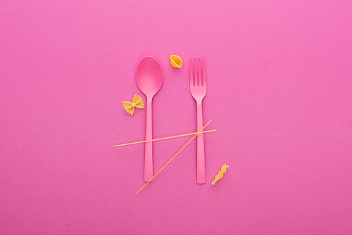 pink plastic spoon and fork and four different kinds of pasta isolated on pink