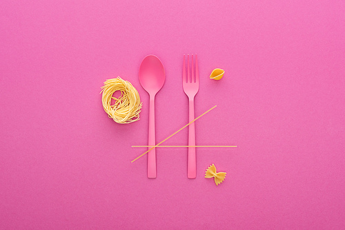 pink plastic spoon and fork near different kinds of pasta isolated on pink