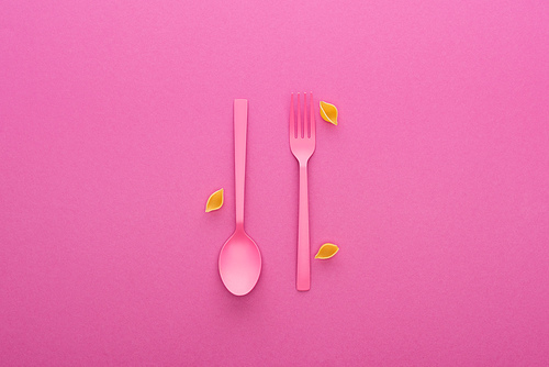 pink plastic fork and spoon upside down and uncooked shells macaroni isolated on pink