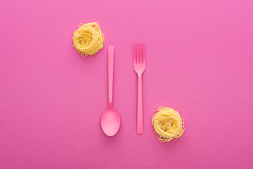 pink plastic fork and spoon upside down near vermicelli pasta on pink background