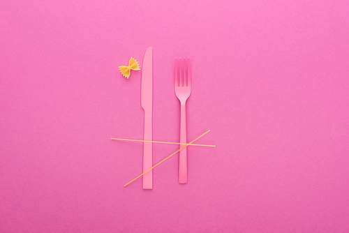 pink plastic knife and fork, spaghetti and uncooked farfalle pasta isolated on pink