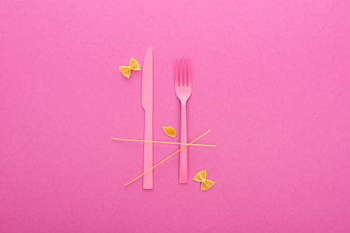 pink plastic knife and fork, spaghetti, uncooked farfalle pasta and shell macaroni isolated on pink