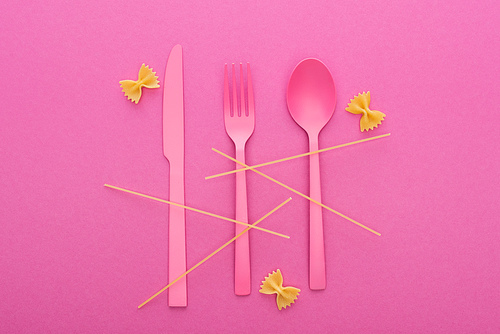 pink plastic knife, fork and spoon, spaghetti and uncooked farfalle pasta isolated on pink