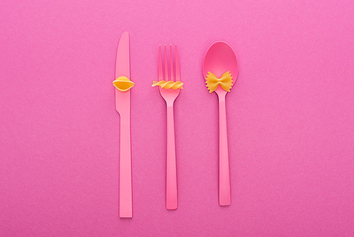 top view of different kinds of pasta on pink plastic cutlery isolated on pink